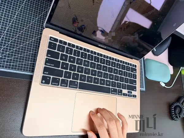 맥북 에어 골드 모델의 트랙패드 위에 세 손가락을 올려 제스처를 시연하는 근접 촬영 사진